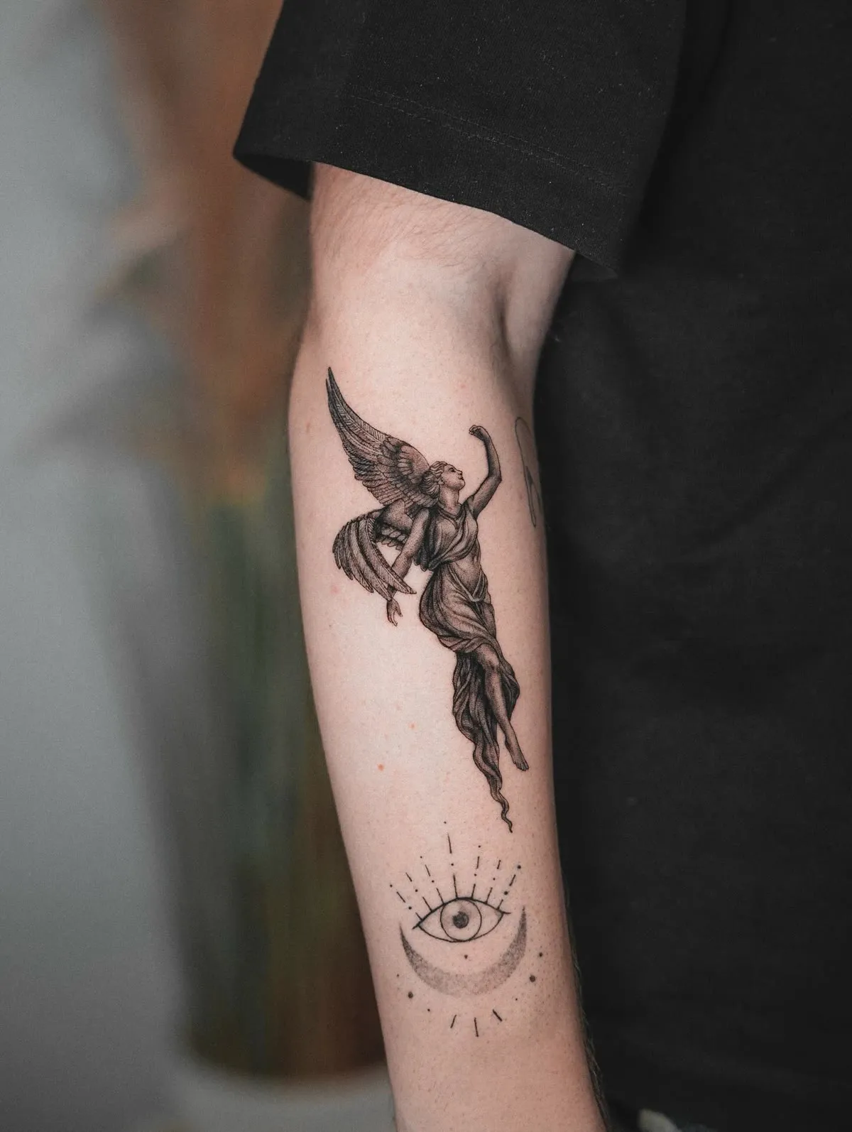 A winged figure holding a sword, drawn along the inside of an upper arm.